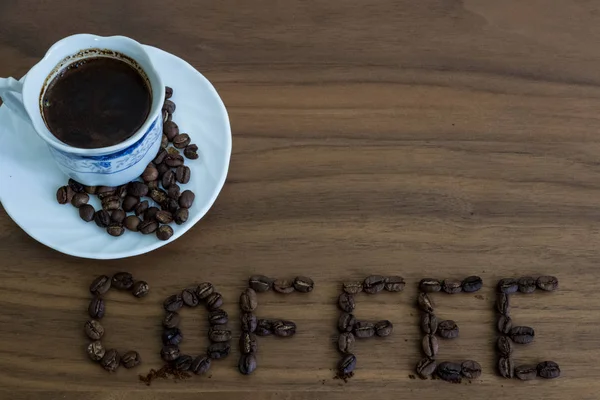Geröstete Kaffeebohnen, verstreut auf dem Tisch und schriftlicher Kaffee, — Stockfoto