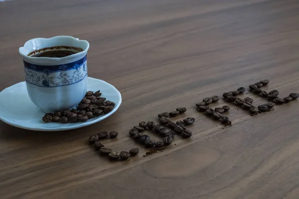 Kavrulmuş kahve çekirdekleri, masanın üzerine dağılmış ve kahve yazılı, — Stok fotoğraf