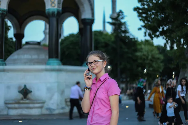 Una giovane ragazza in piedi sulla strada, nel parco, utilizzando un cellulare — Foto Stock