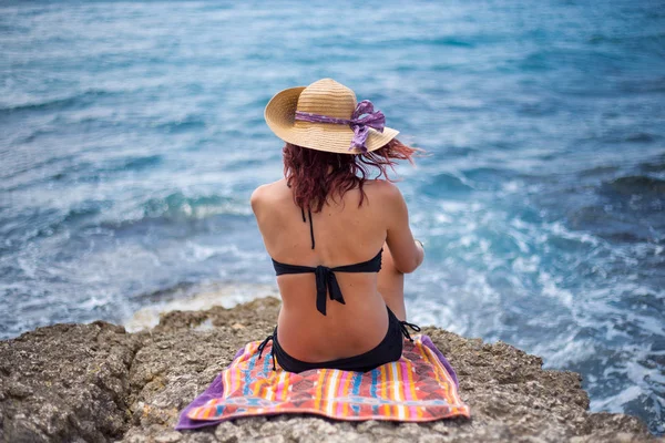 En ung flicka i en bikini och en stråhatt på stranden njuter den — Stockfoto