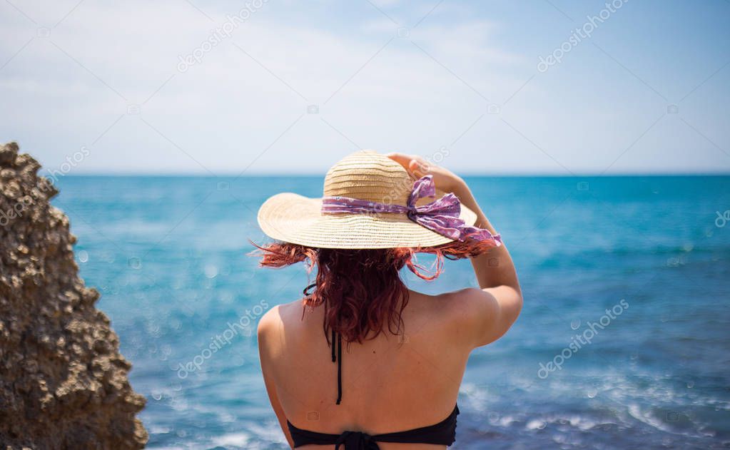 A young girl in a bikini and a straw hat on the beach enjoys the