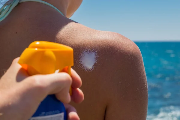 Applying sun cream sunscreen on a shoulder of a woman for tannin