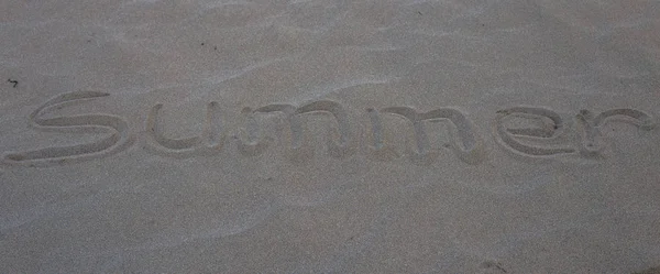 A palavra verão escrito na areia cinza na praia no ouvido — Fotografia de Stock