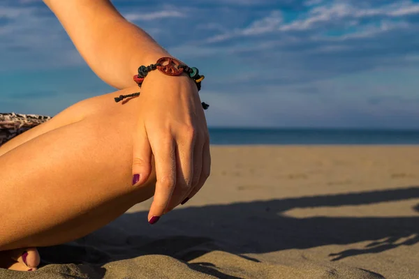 Женщина сидит на пляже с крупным планом руки с браслетом и — стоковое фото