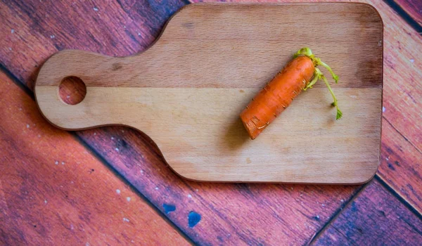 Wooden cutting board with orange fresh carrot on the wooden back