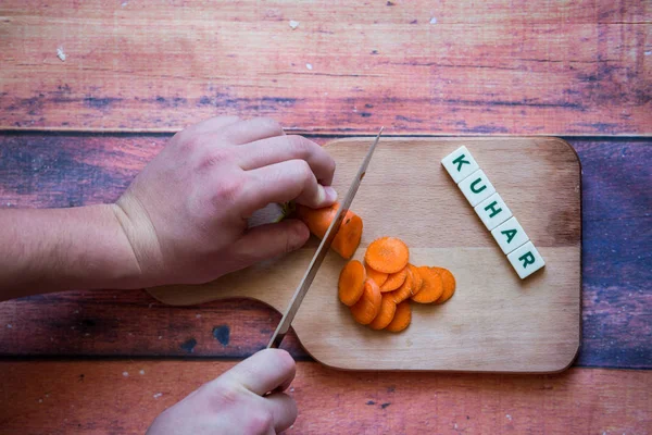 Chef is cutting carrot on a wooden cutting board with sharp knif