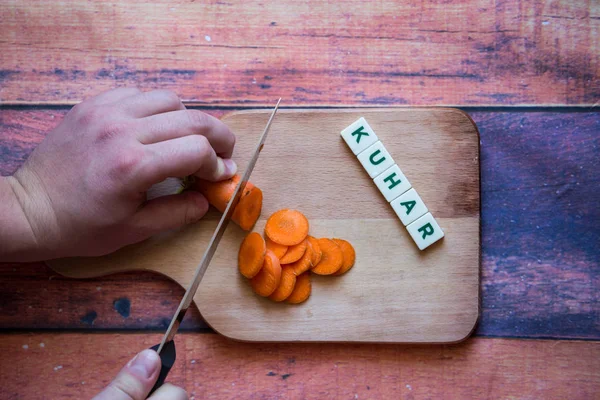 Chef is cutting carrot on a wooden cutting board with sharp knif