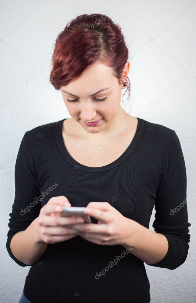 A young girl holds a cell phone and writes messages, a smile on 