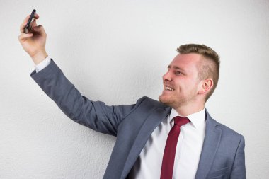 A young businessman in a suit, using a front camera of a mobile 