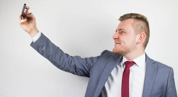 Młody biznesmen w garniturze, przy użyciu kamery przedniej w telefonie — Zdjęcie stockowe