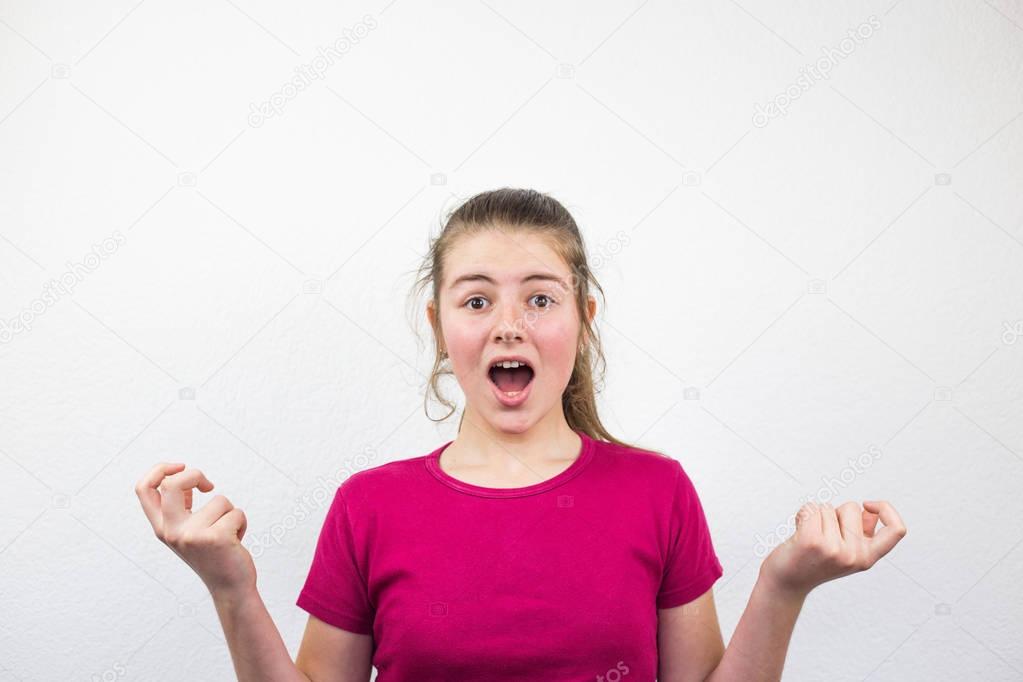 Young and beautiful blonde teenage girl yelling and shouting in frustration and fear with the white background and lively facial expression in studio.