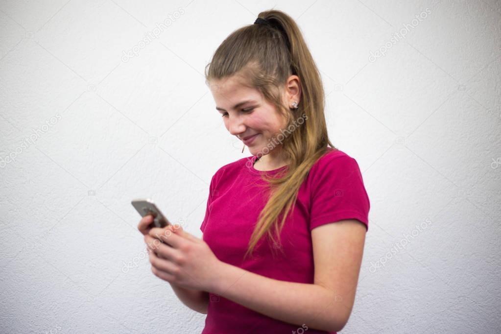 Young and blonde teenage girl typing an email message on smart phone and smiling happy to receive a notification on social media.