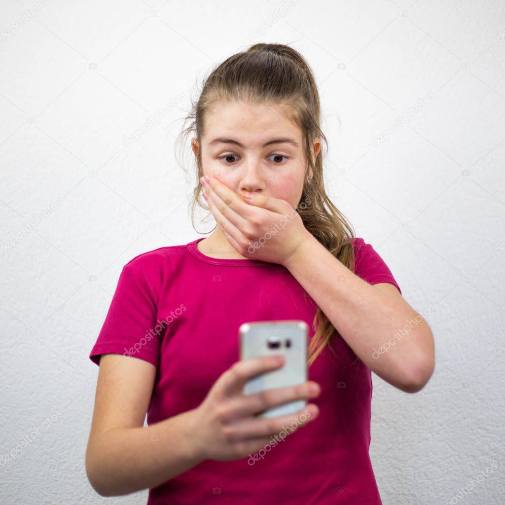 Looking at the phone in excitement, shock and fear with hand over her mouth and eyes wide open, beautiful teenage girl in the studio white background.