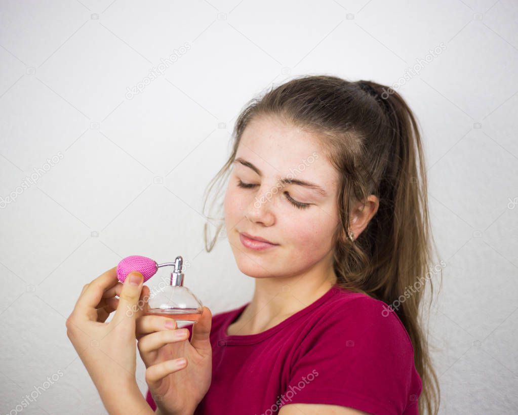 Blond teenage young kid girl putting perfume on her long neck wxposed and a head high blond hair and pink container of nice smell in the studio.