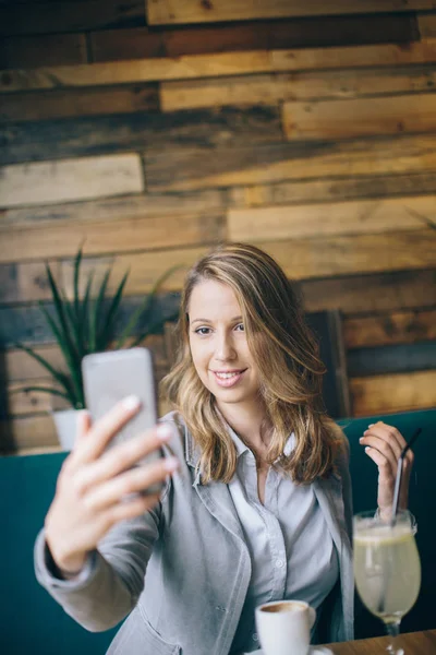 Девушка сидит за столом и использует смартфон — стоковое фото