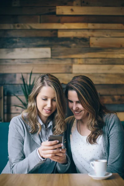 Девушки сидят за столом и используют смартфон — стоковое фото