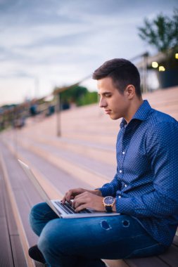 Merdivenlerde oturan ve dizüstü bilgisayar kullanarak bir adam