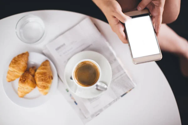 スマートフォンのある女性とコーヒーとクロワッサンの朝食 — ストック写真