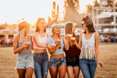 Güzel görünümlü genç kadınlar bira içiyor ve festivalde hafta sonları müzik başlıyor. 