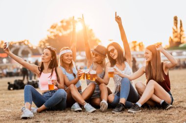 Müzik festivalinde çimenlerin üzerinde içkili gülümseyen kızlar. 