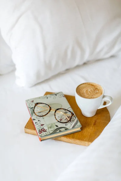 white cup of morning coffee with book and glasses on white bed background