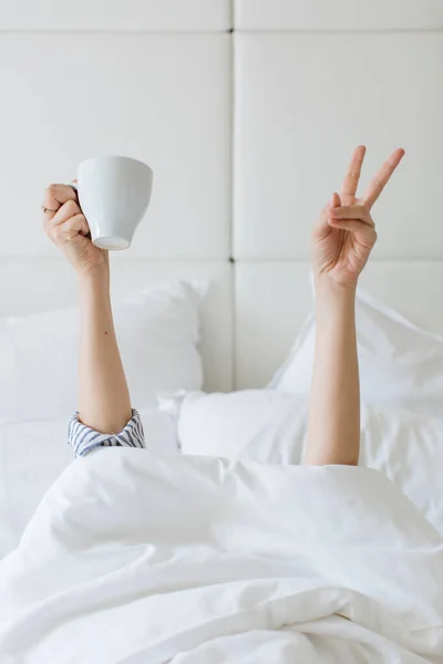Person Mit Weißer Tasse Und Zwei Erhobenen Fingern Weißem Bett — Stockfoto