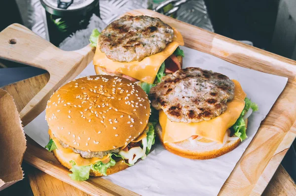 Pyszne hamburgery, pyszne fast food, Sałatka jarzynowa, ketchup i ser jest nadziewane w pyszny chleb na drewnianej tacy. — Zdjęcie stockowe