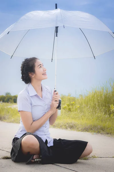 A menina asiática está sorrindo na estrada no prado e no guarda-chuva e olhando para as flores de grama em sua mão — Fotografia de Stock