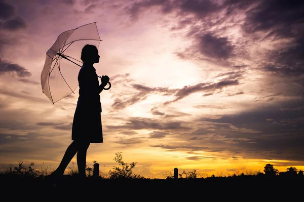 As meninas tristeza estilo silhueta andando sozinho ao ar livre e guarda-chuva em sua mão com céu nublado e sol da noite — Fotografia de Stock