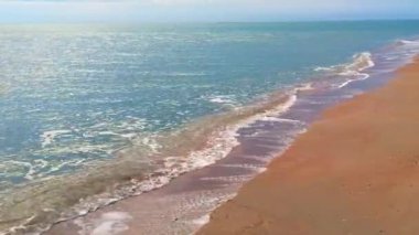 Issız sahil, mavi su ve sarı kumu büyük, ağır bulutları ile bulutlu gökyüzü altında deniz ya da okyanus dalgaları