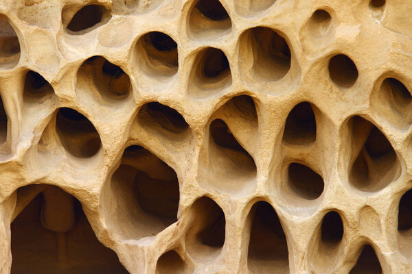 Ветер размыл желтую известняковую гору с большим количеством маленьких отверстий
