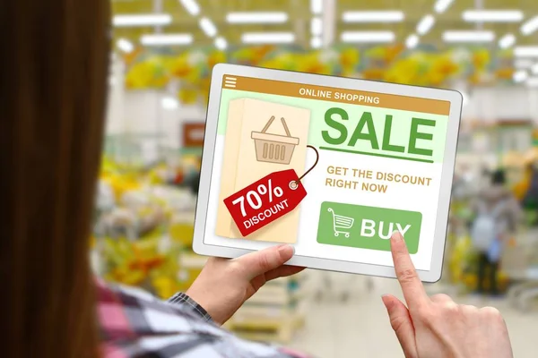 Sale and discount concept, girl holds the digital tablet on blurred shop background