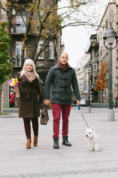 Glückliches Paar, das mit Hund in der Stadtstraße spazieren geht und in die Kamera blickt — Stockfoto