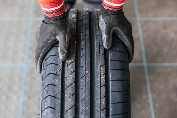 Mãos mecânicas empurrando um pneu preto — Fotografia de Stock