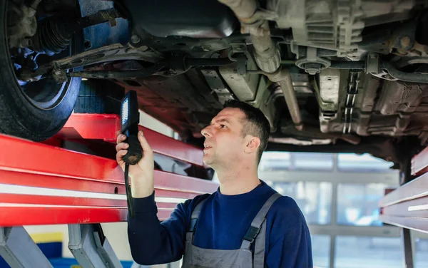 Mecânico examinando carro usando lanterna — Fotografia de Stock