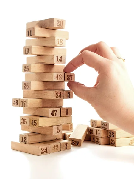 Blokken van spel jenga geïsoleerd op een witte achtergrond. Verticale toren geheel en in het spel. Houten blokken in de stapel met cijfers cijfers op lichaam. vrouwelijke hand neemt blokken. — Stockfoto