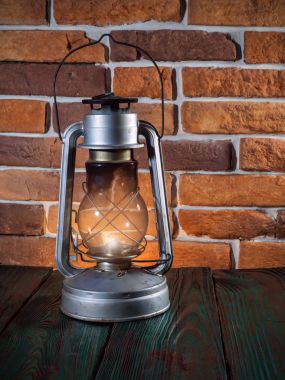 Natürmort gaz lambası yanar ahşap masaüstü taş tuğla zemin üzerine.