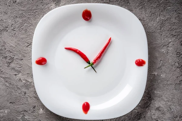 Hot chilli pepper on white plate with decor ketchup concept idea imitation clock time meal breakfast lunch snack dinner