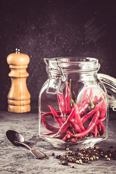Red hot chilli pepper paprika in glass jar and peppers seed ball and pepper mill on stone table Ingredient for Mexican cooking, Trendy toned image in rustic style