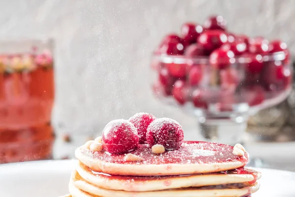 De zelfgemaakte cake pannenkoeken in stapel versierd met bessen bevroren cherry bestrooi met suiker poeder op witte plaat — Stockfoto