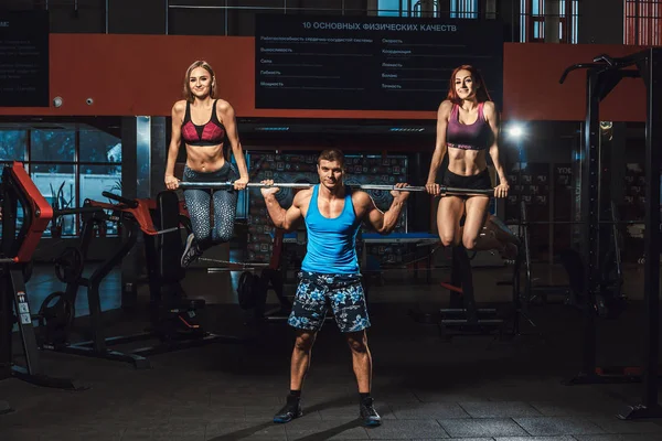 athletic man lifts barbell with two girls as weight and girls hanging From barbell. barbell with two girls on it