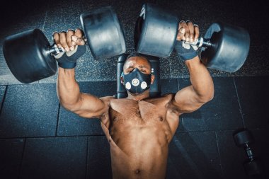 Halter kaldırma ve onun göğüs görüşüne yukarıdan çalışma maskeli Afro-Amerikan atletik adam. zenci göğüs dumbell yakın çekim ile egzersiz yaparak spor salonunda