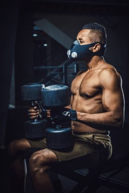 oturma ve bekleyen ve kendisi de aynanın önünde halter kaldırma önce seyir maskeli Afro-Amerikan atletik adam. zenci dumbbells ile spor salonunda