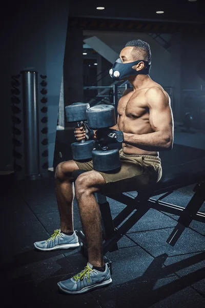 oturma ve bekleyen ve kendisi de aynanın önünde halter kaldırma önce seyir maskeli Afro-Amerikan atletik adam. siyah adam önce egzersiz hazırlama dumbbells ile spor salonunda