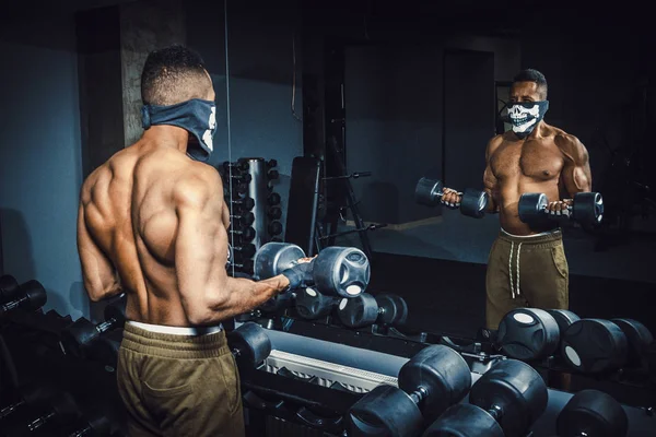 Halter kaldırma ve onun pazı salonunda ayna önünde çalışma Afro-Amerikan atletik bir adam. pazı dumbbells ile egzersiz yaparak spor salonunda zenci adam