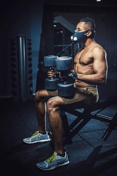 oturma ve bekleyen ve kendisi de aynanın önünde halter kaldırma önce seyir maskeli Afro-Amerikan atletik adam. zenci dumbbells ile spor salonunda