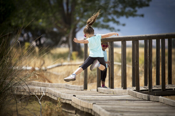 Jovial kid jumping in mid-air on wooden path