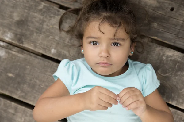 Triste petite fille en t-shirt bleu couché sur un fond en bois — Photo
