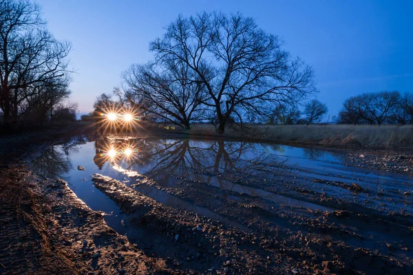 Auto poblíž louži večer s reflektory na — Stock fotografie