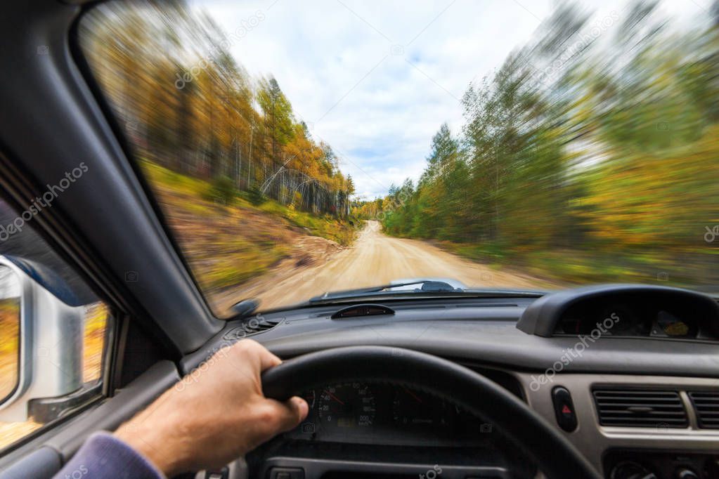 Car drive trough autumn forest by a dirt road
